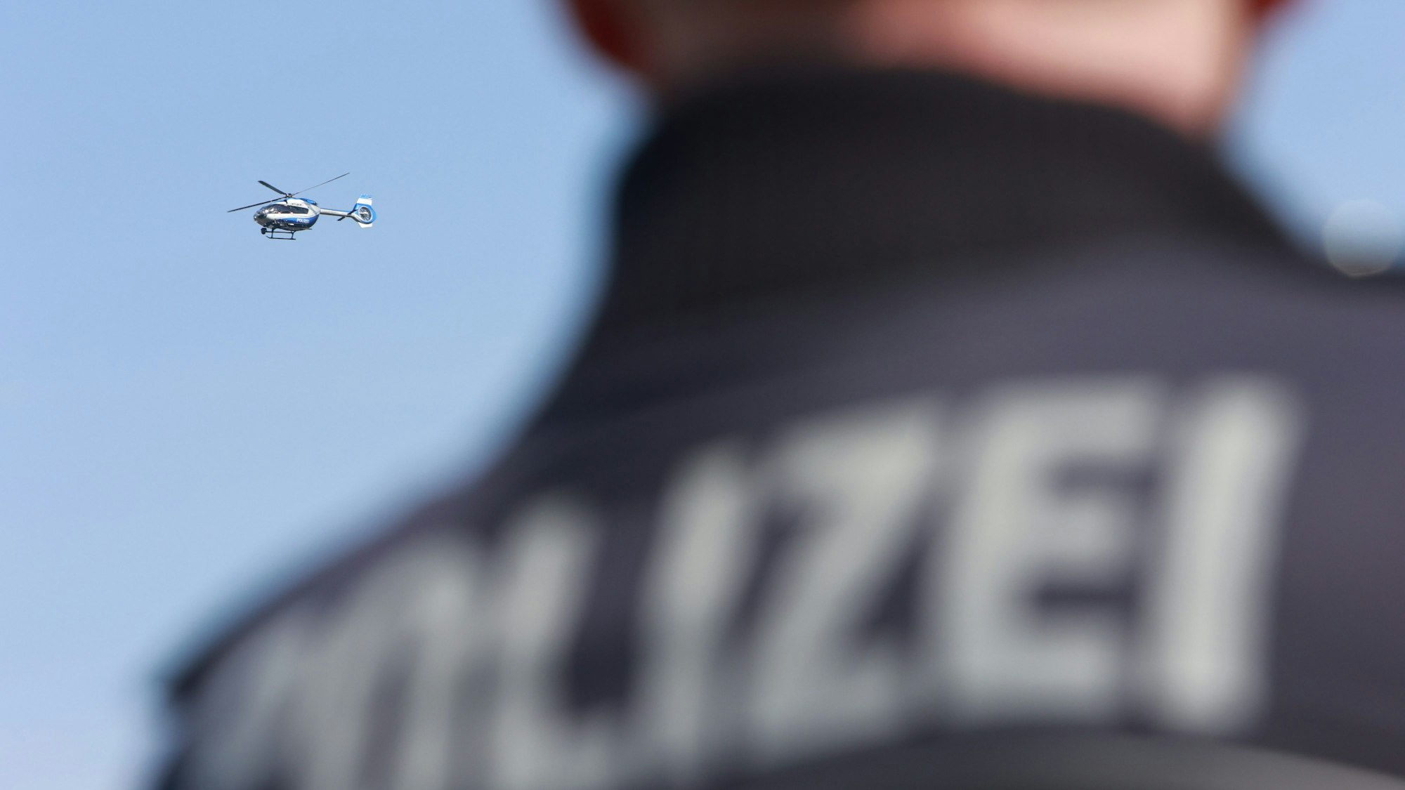 Ein Polizeihubschrauber fliegt am Himmel, im Vordergrund steht ein Polizist.