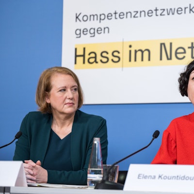 Lisa Paus und Elena Kountidou sitzen an einem Tisch, vor ihnen stehen Namensschilder und Mikrofone auf dem Tisch. Im Hintergrund die Aufschrift "gegen Hass im Netz".