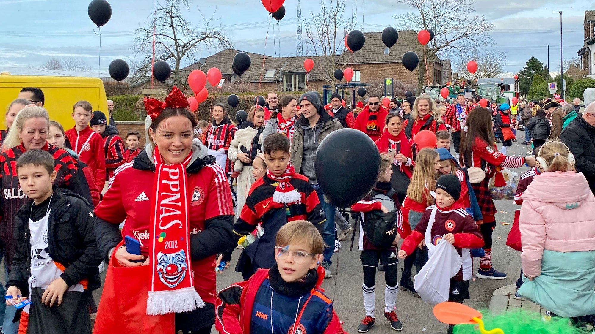 Kinder und Jugendliche in Fußballtrikots und mit schwarzen und roten Ballons in den Händen.