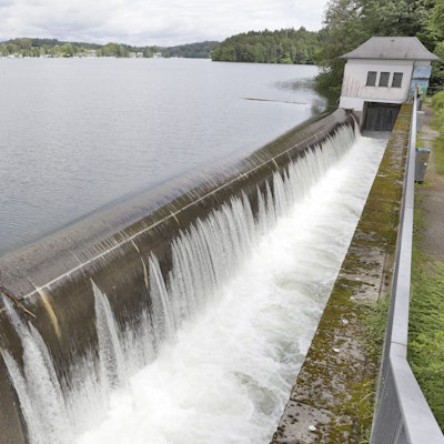 Wasseroberfläche einer Talsperre, Wasser läuft über eine Kante und stürzt in ein kleineres Becken.