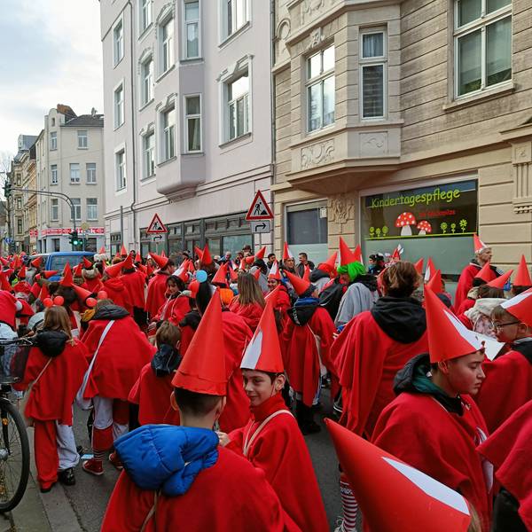 Kinder in roten Kostümen und Spitzhüten stehen als Teil des Veedelszugs auf einer Mülheimer Straße.