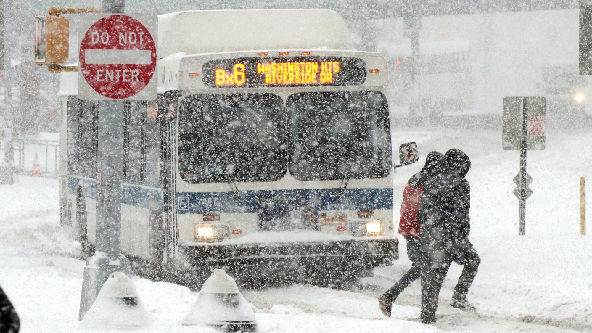 Passanten gehen bei starkem Schneefall über eine Straße in New York, im Hintergrund fährt ein Bus durch den massiven Schneefall. (Archivbild)