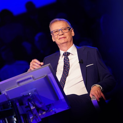 „Wer wird Millionär“-Moderator Günther Jauch sitzt während der Quizshow des Kölner TV-Senders RTL auf seinem Stuhl am Pult uns grinst ins Publikum.