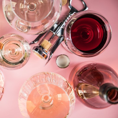 Mehrere Gläser Wein, eine Flasche und ein Korkenzieher liegen auf einer Unterlage.