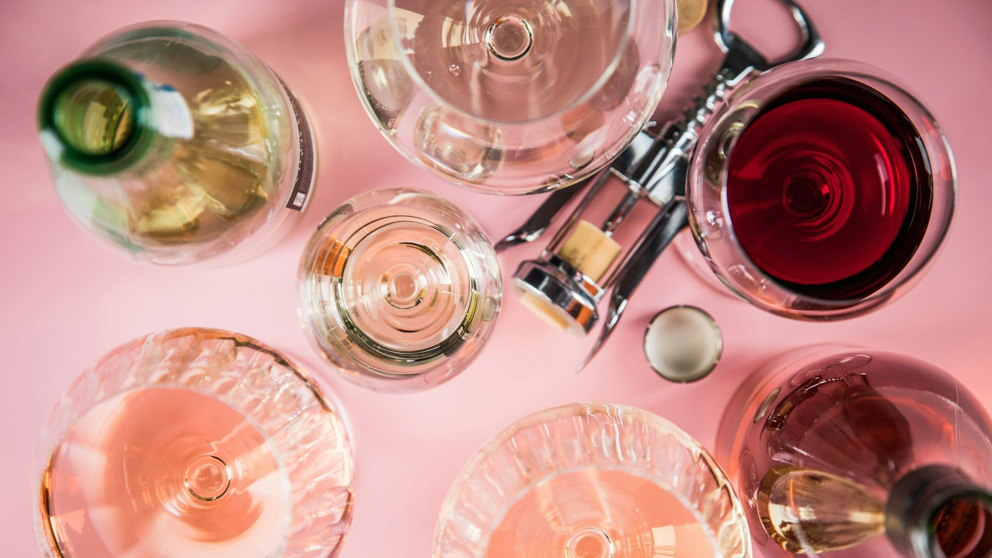 Mehrere Gläser Wein, eine Flasche und ein Korkenzieher liegen auf einer Unterlage.