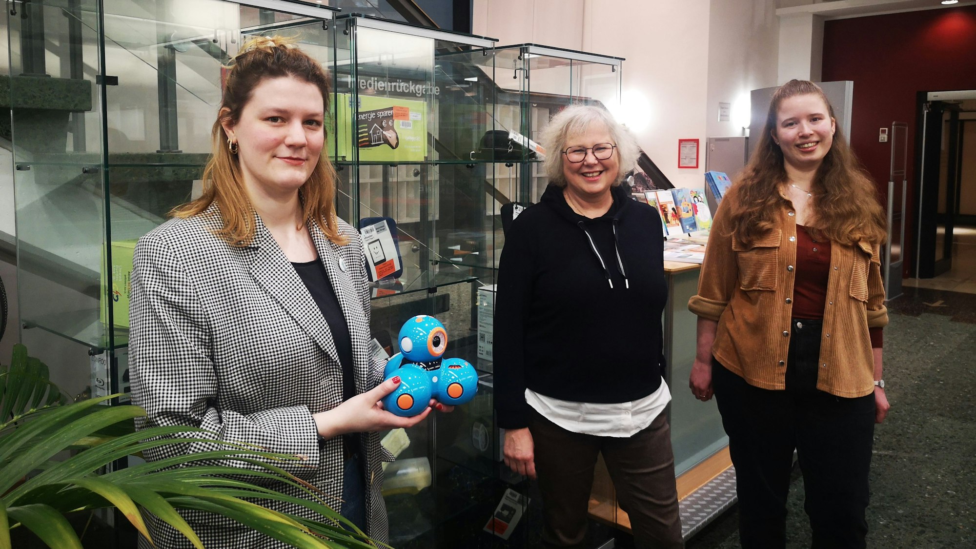 Auch Programmier-Roboter können ausgeliehen werden. Verena Mayer (v.l.), stellv. Leiterin der Stadtbibliothek, Eva-Marie Urban, Leiterin, und Cassandra Hennes, Öffentlichkeitsbeauftragte der Bibliothek, vor den Vitrinen mit Geräten für Erwachsene.