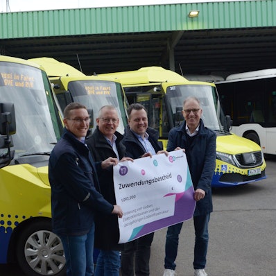 Norbert Reinkober, Marcel Frank, Anno Schichler-Koep und Sacha Reichelt stehen vor mehrern blau-gelben Bussen und halten einen Zuwendungsbescheid in der Hand.
