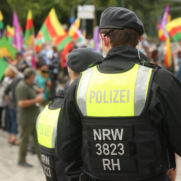 Ein Polizist steht mit dem Rücken zur Kamera vor einer Gruppe Demonstranten.