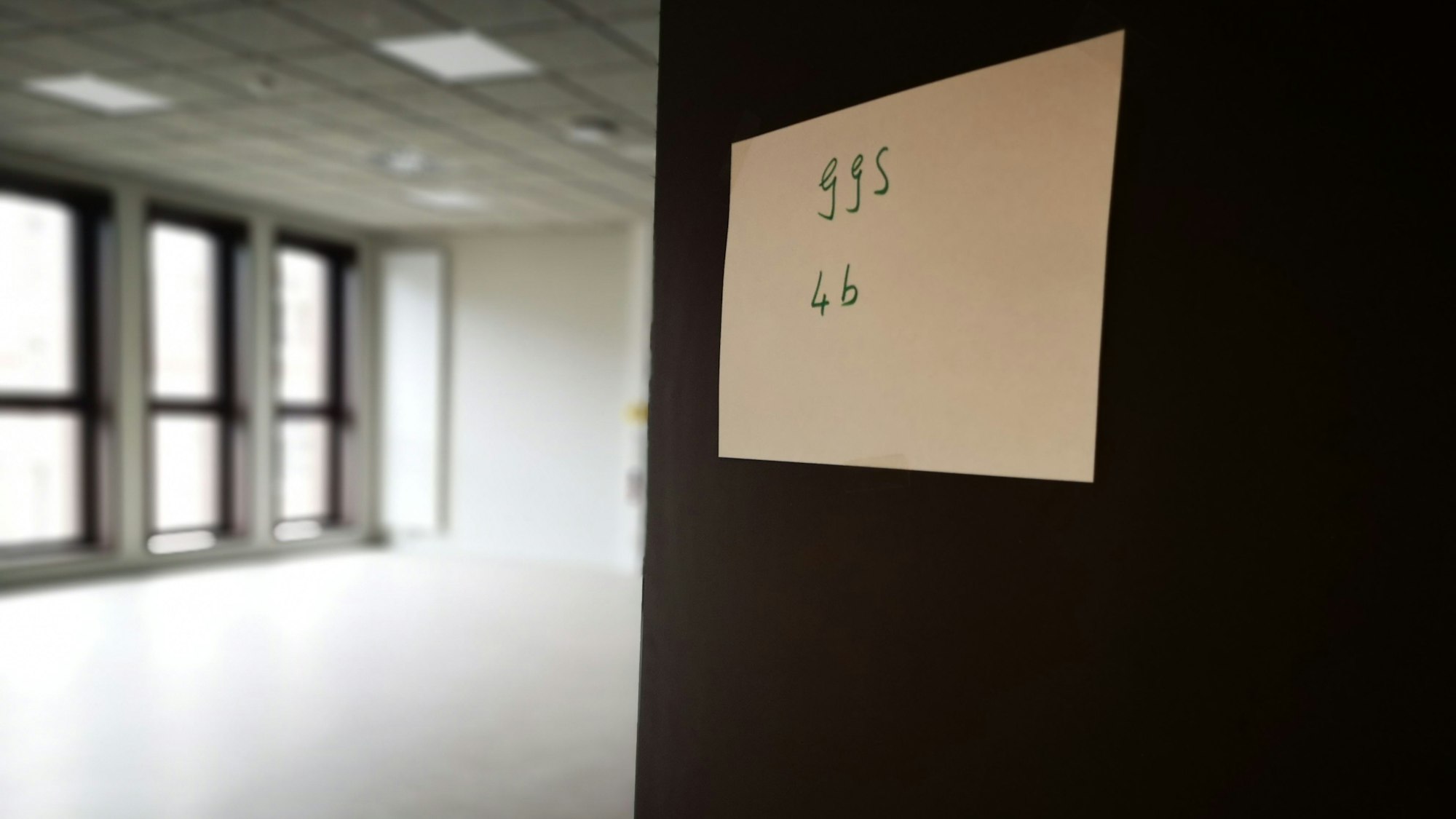 Eine Tür mit einem Papierschild öffnet sich in einen Klassenraum mit vielen Fenstern.