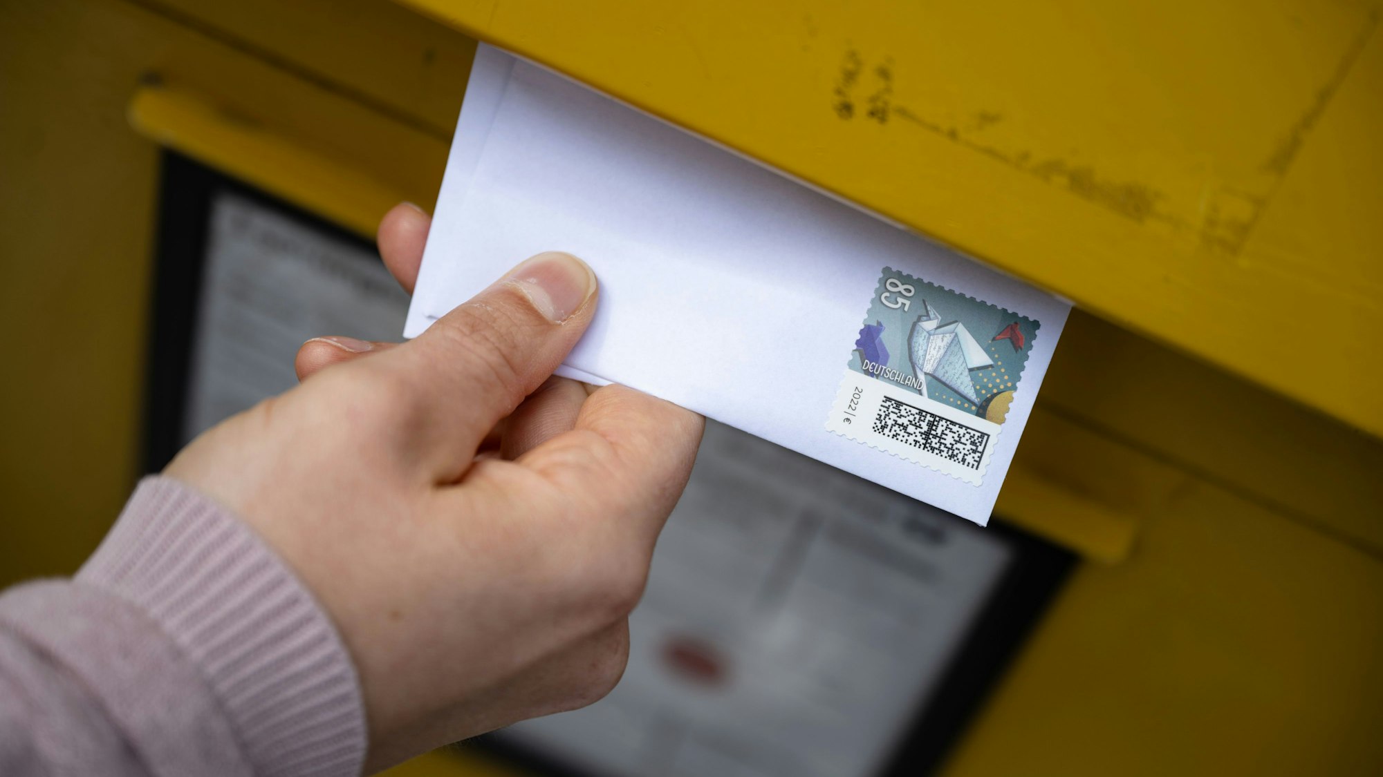 Eine Frau wirft einen Standardbrief in einen Briefkasten.
