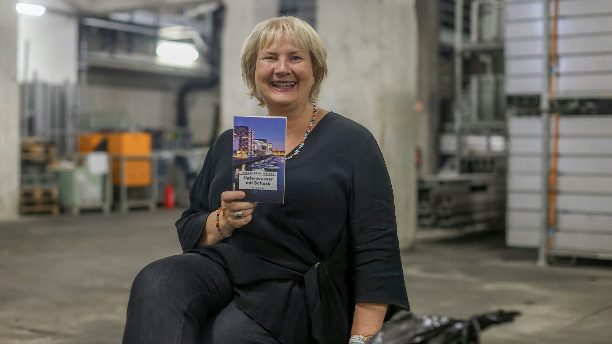 Dagmar Maria Toschka sitzt mit ihrem Krimi in einem Raum in der Deutzer Brücke.