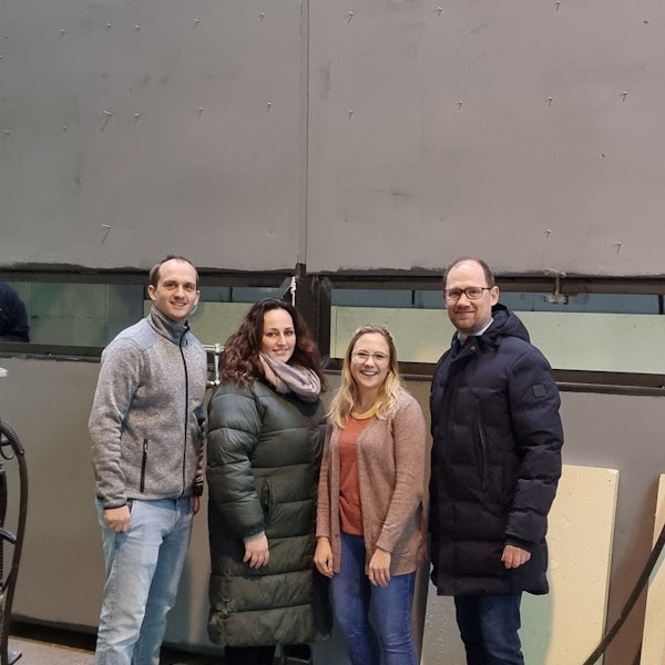 Die vier Personen stehen vor einem künftigen Schwimmcontainer.