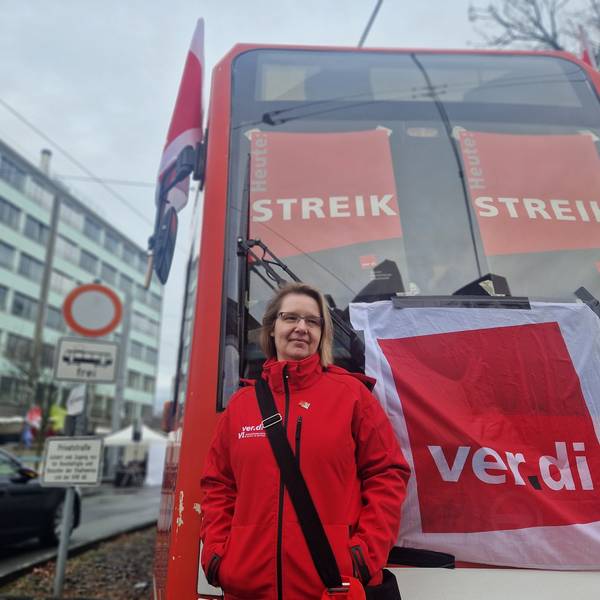 Eine Frau steht vor einer Straßenbahn der KVB. Darauf sind Streik-Plakate zu sehen.