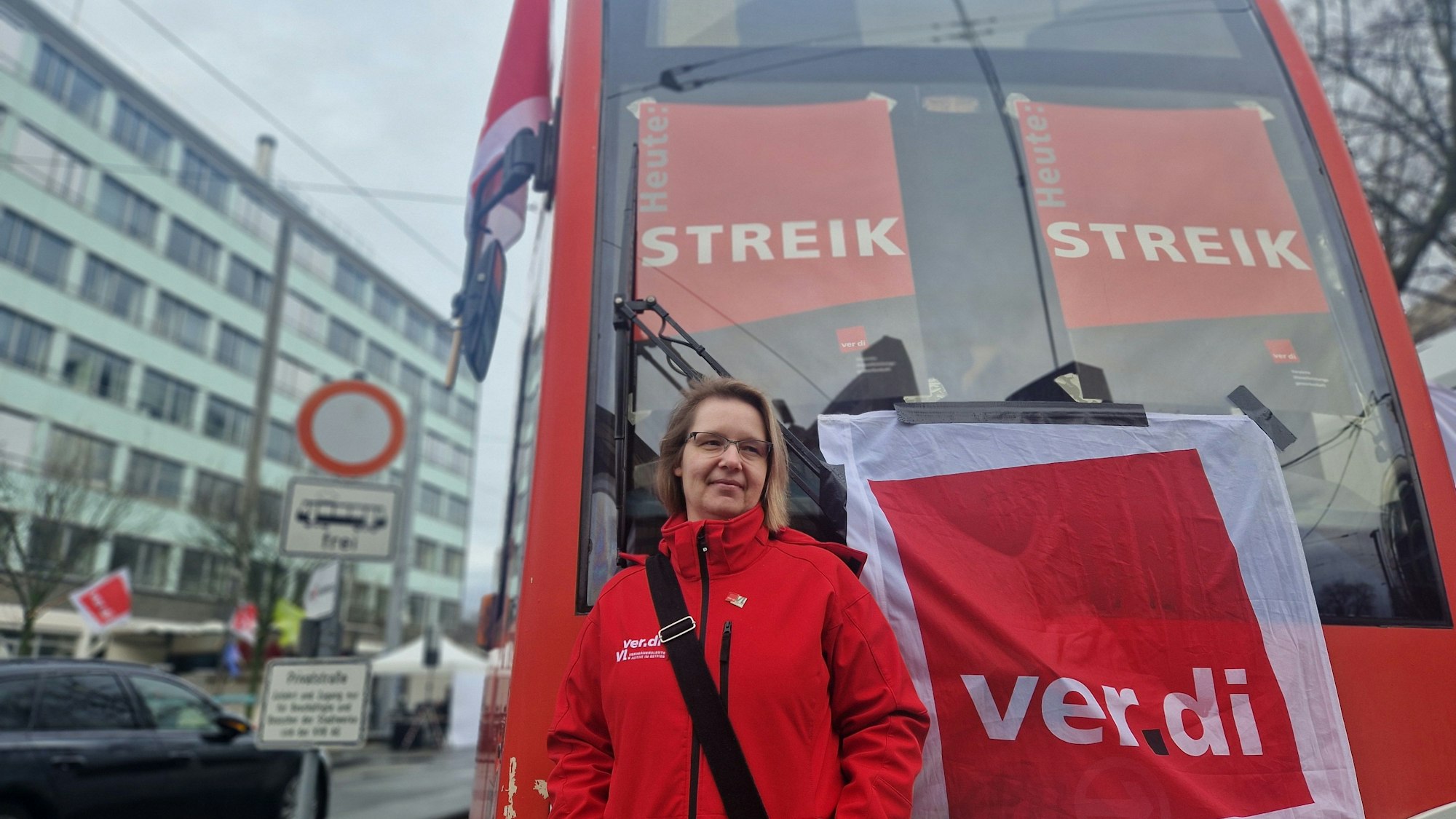 Eine Frau steht vor einer Straßenbahn der KVB. Darauf sind Streik-Plakate zu sehen.