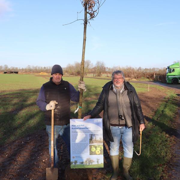 Zwei Männer halten ein Plakat und einen Baum.
