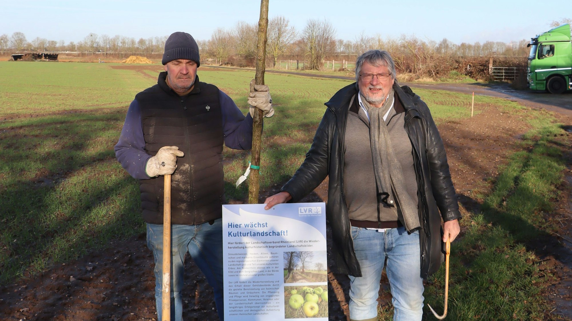 Zwei Männer halten ein Plakat und einen Baum.