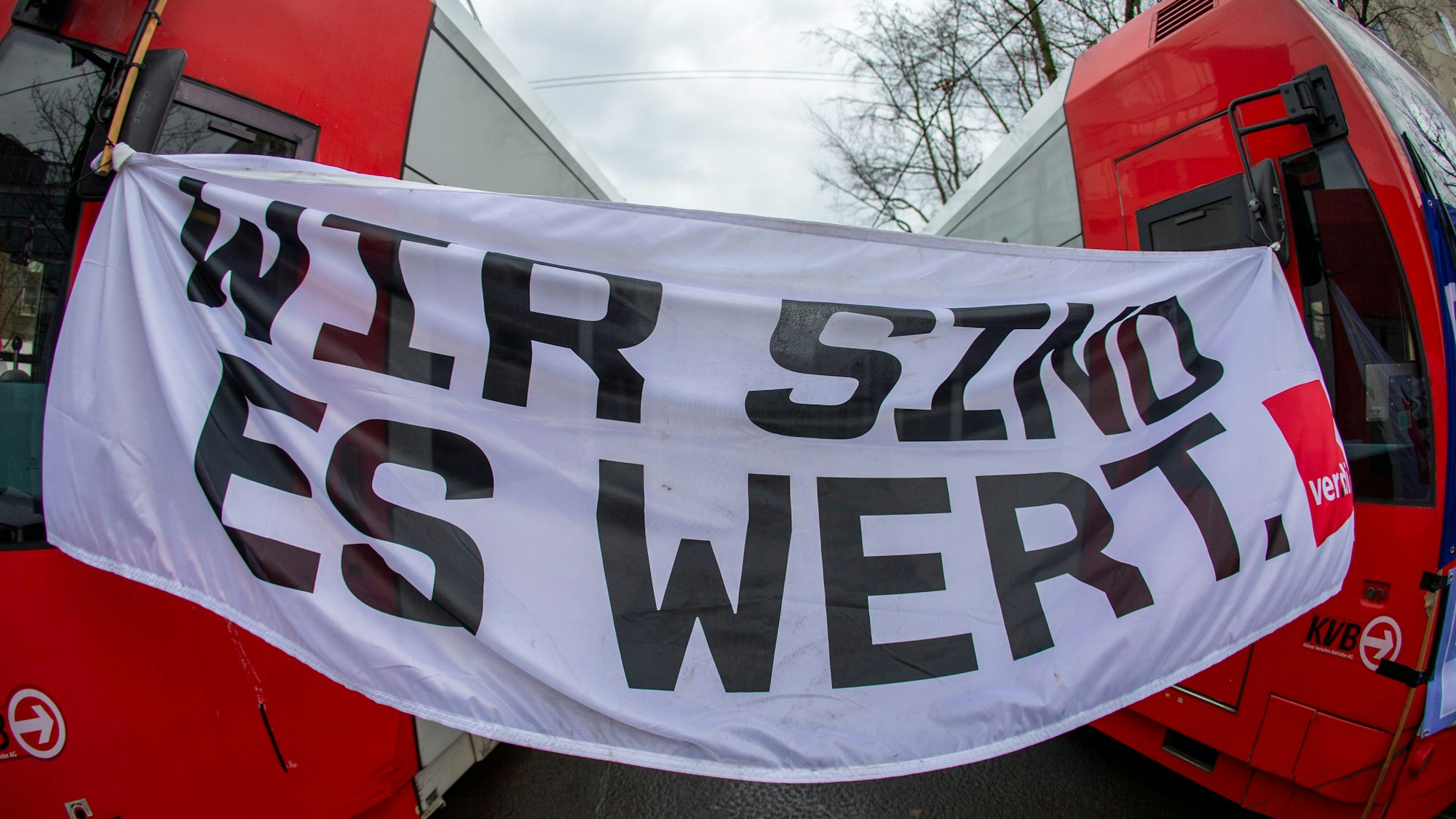 Ein Banner zwischen zwei KVB Bahnen, darauf steht: Wir sind es wert.