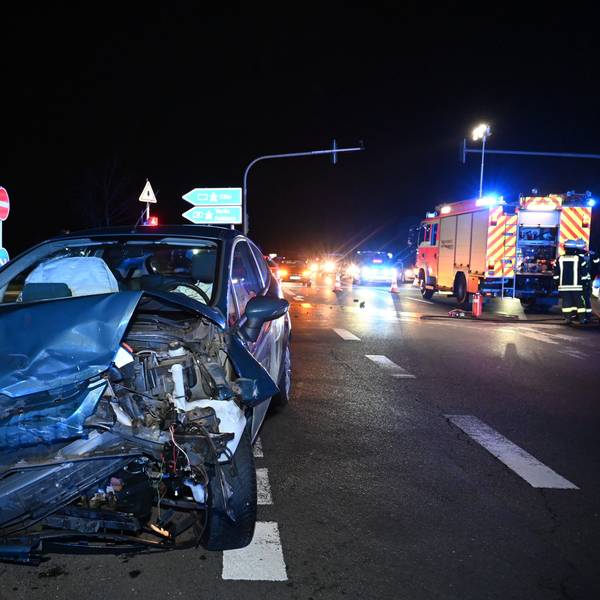 Ein blauer Pkw steht schwer beschädigt auf einer Straßenkreuzung in der Nacht. Die vordere linke Seite ist verbogen und kaputt.