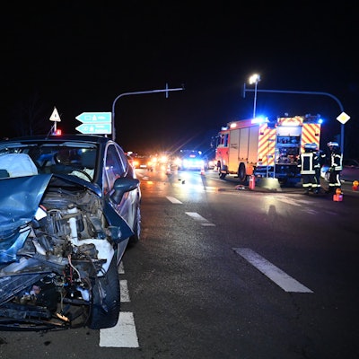 Ein blauer Pkw steht schwer beschädigt auf einer Straßenkreuzung in der Nacht. Die vordere linke Seite ist verbogen und kaputt.
