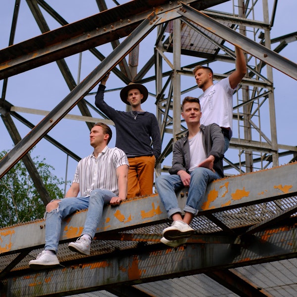 Ein Gruppenfoto einer Band. Die vier jungen Männer sind auf ein Gerüst geklettert.