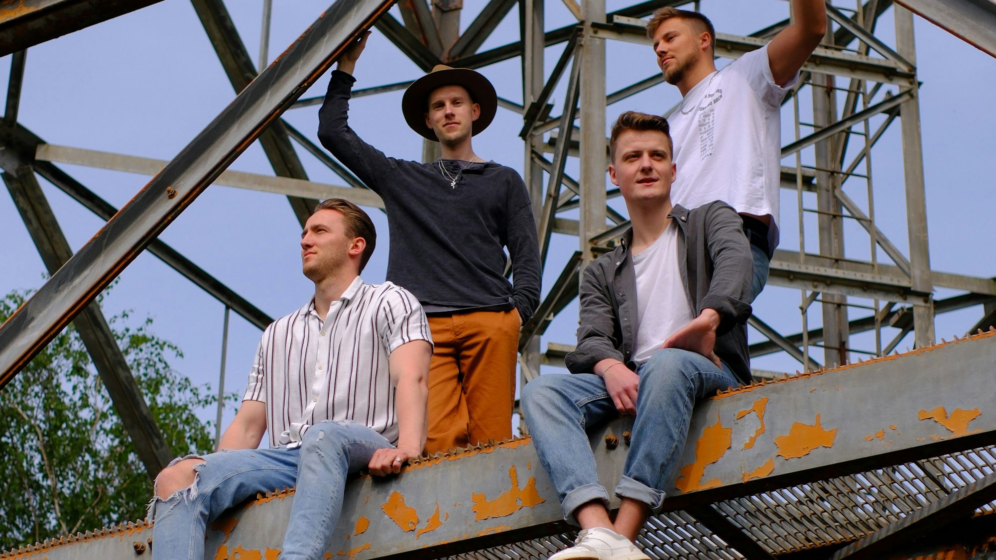 Ein Gruppenfoto einer Band. Die vier jungen Männer sind auf ein Gerüst geklettert.