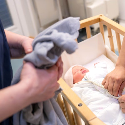 Ein Säugling liegt in einem Bett und wird von Hebammen versorgt.