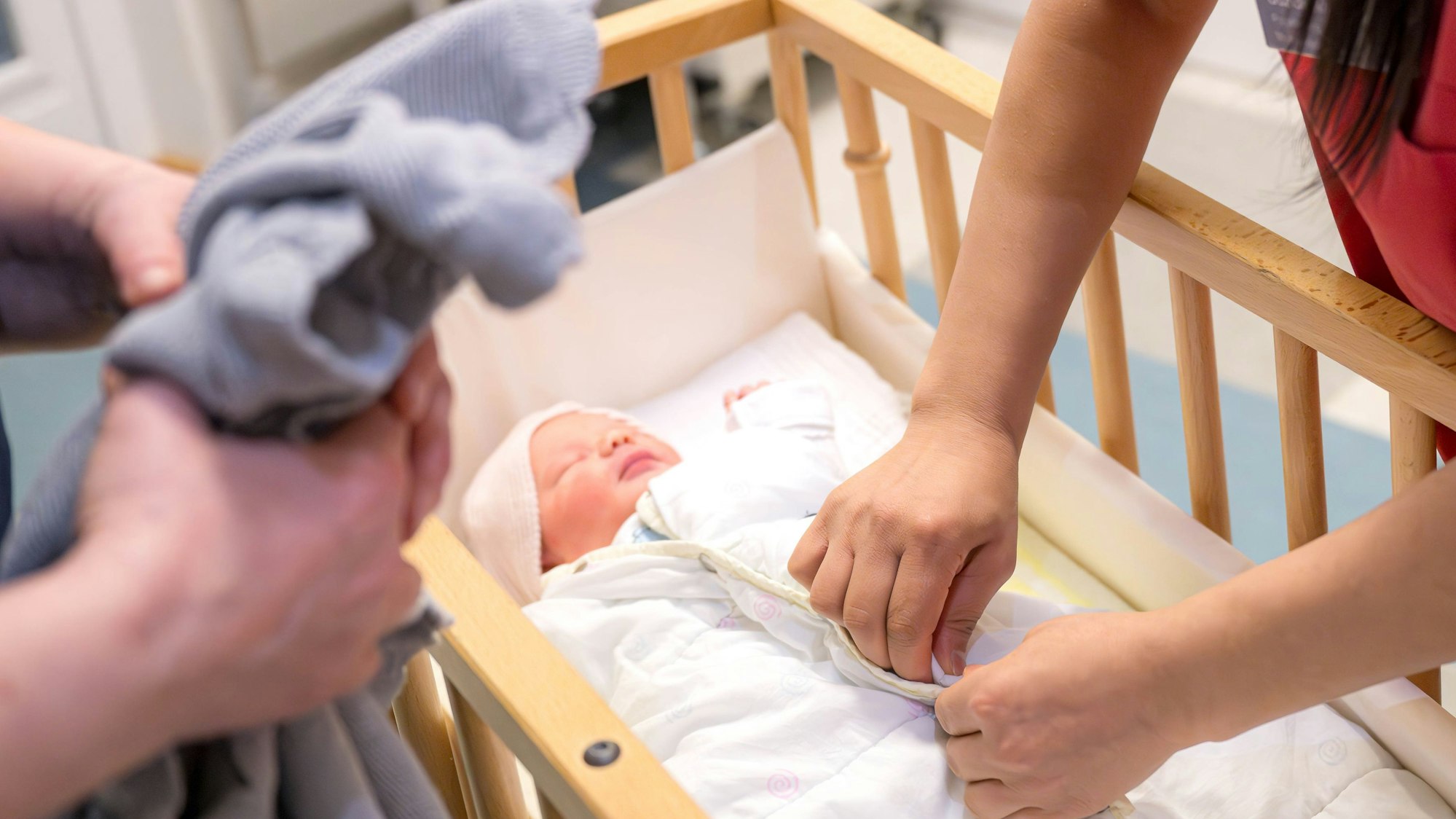 Ein Säugling liegt in einem Bett und wird von Hebammen versorgt.