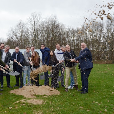 Die Teilnehmerinnen und Teilnehmer werfen mit Spaten Sand in Luft.