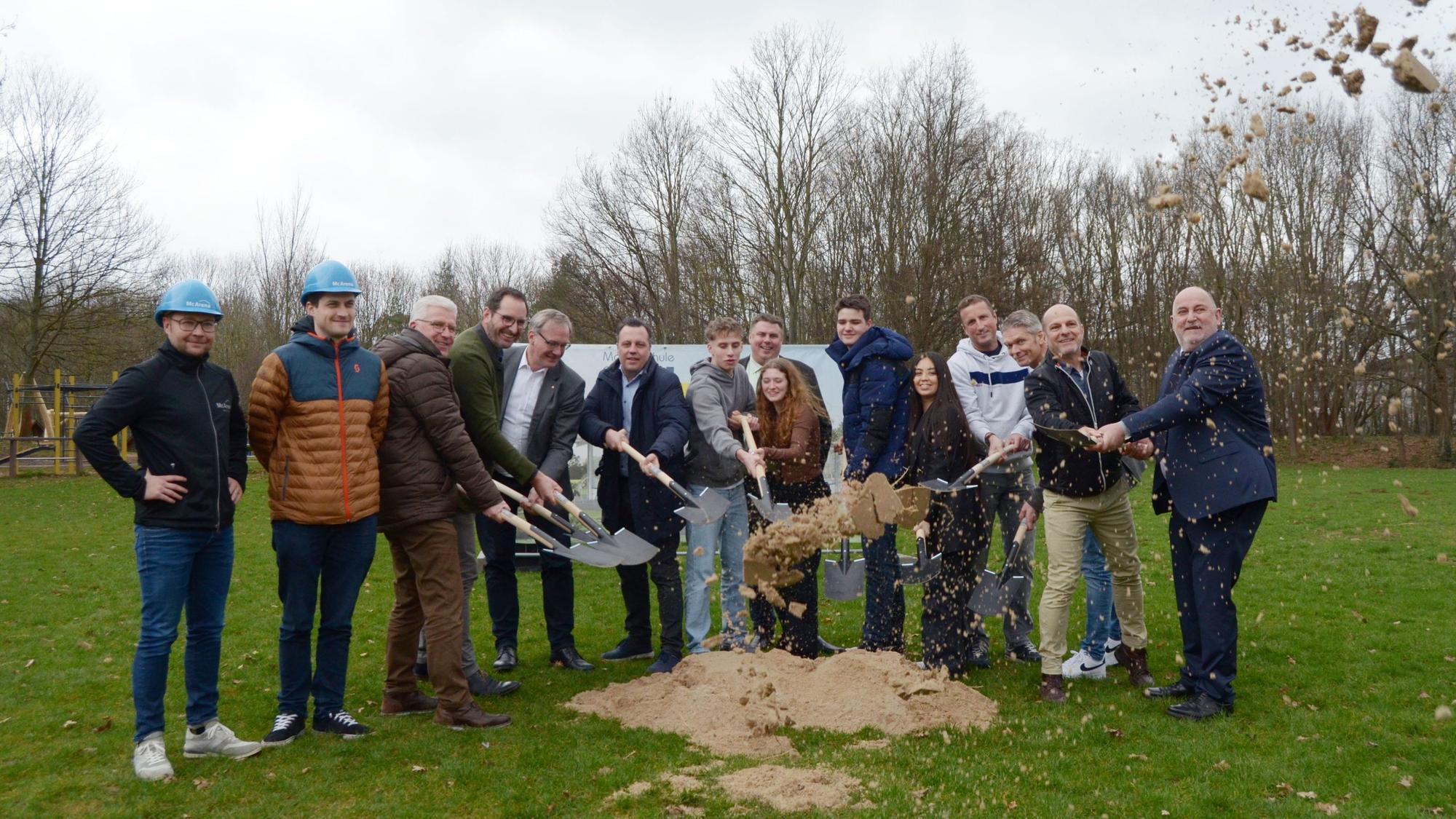 Die Teilnehmerinnen und Teilnehmer werfen mit Spaten Sand in Luft.