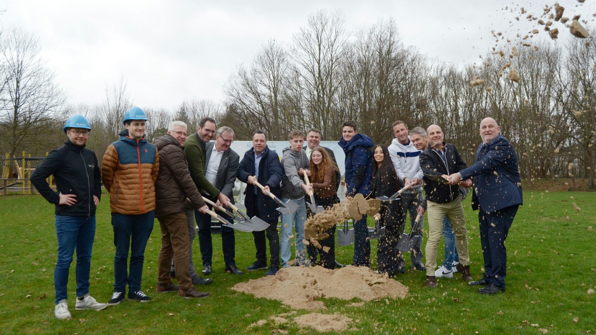 Die Teilnehmerinnen und Teilnehmer werfen mit Spaten Sand in Luft.