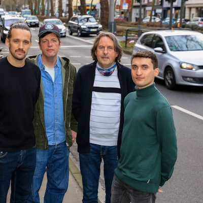 Fünf Männer stehen vor einer vielbefahrenen Straße.