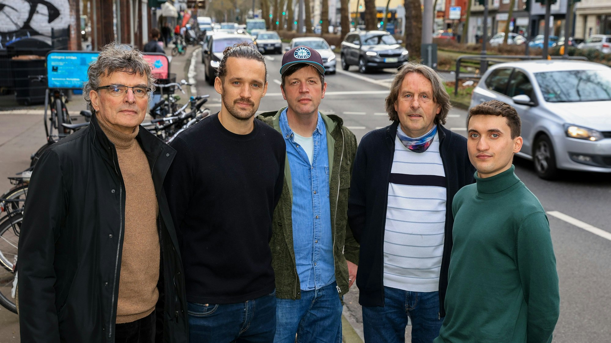 Fünf Männer stehen vor einer vielbefahrenen Straße.