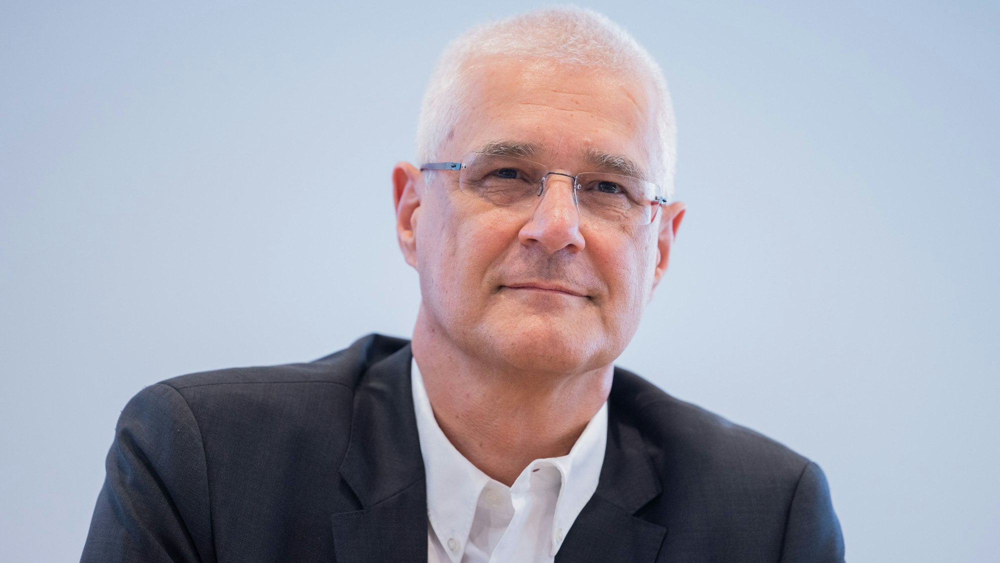 Ingo Morell, Präsident der Krankenhausgesellschaft Nordrhein-Westfalen schaut in Nahaufnahme vor einem grauen Hintergrund in die Ferne.