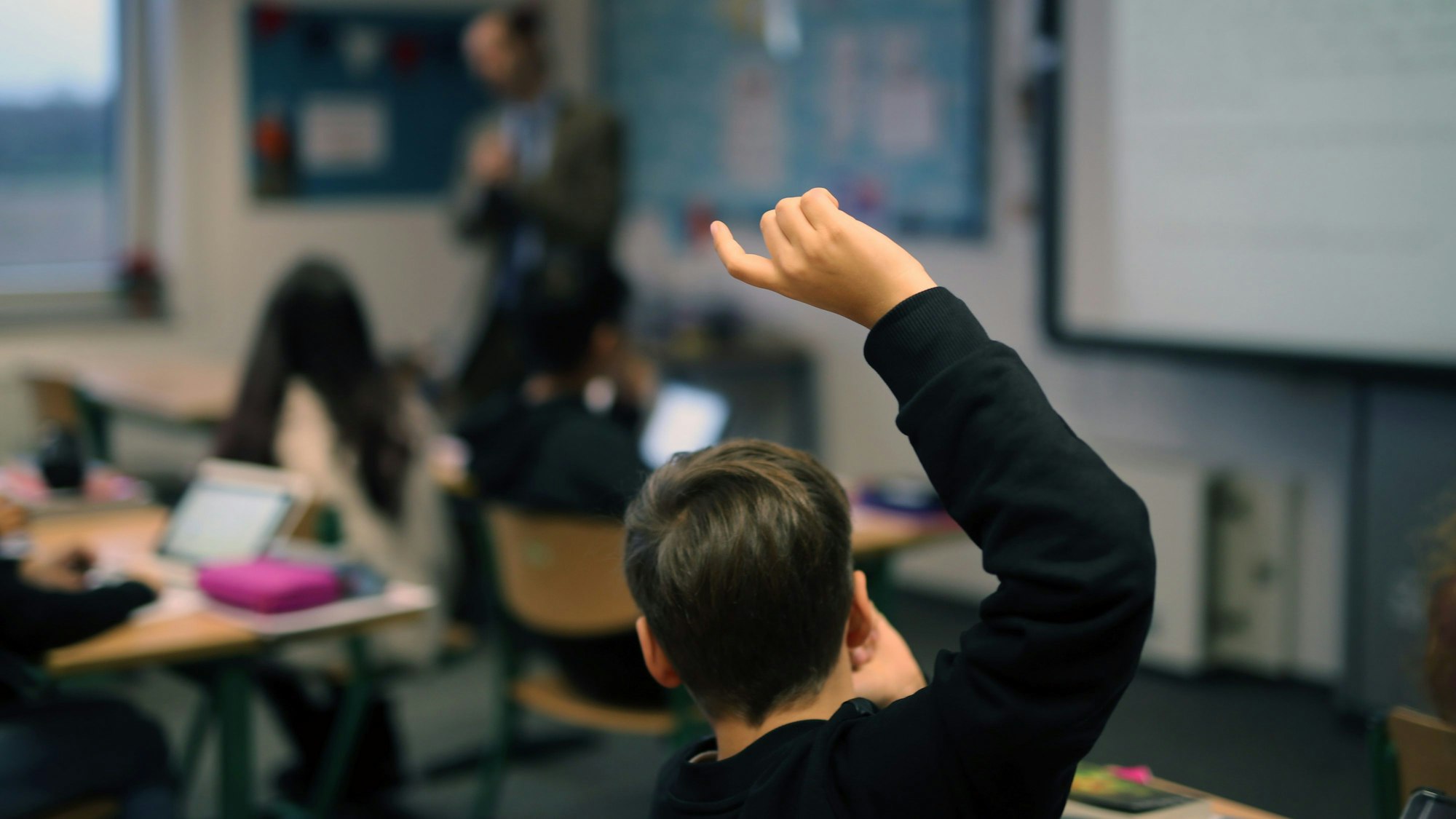 Ein Schüler hebt im Unterricht seine Hand hoch.