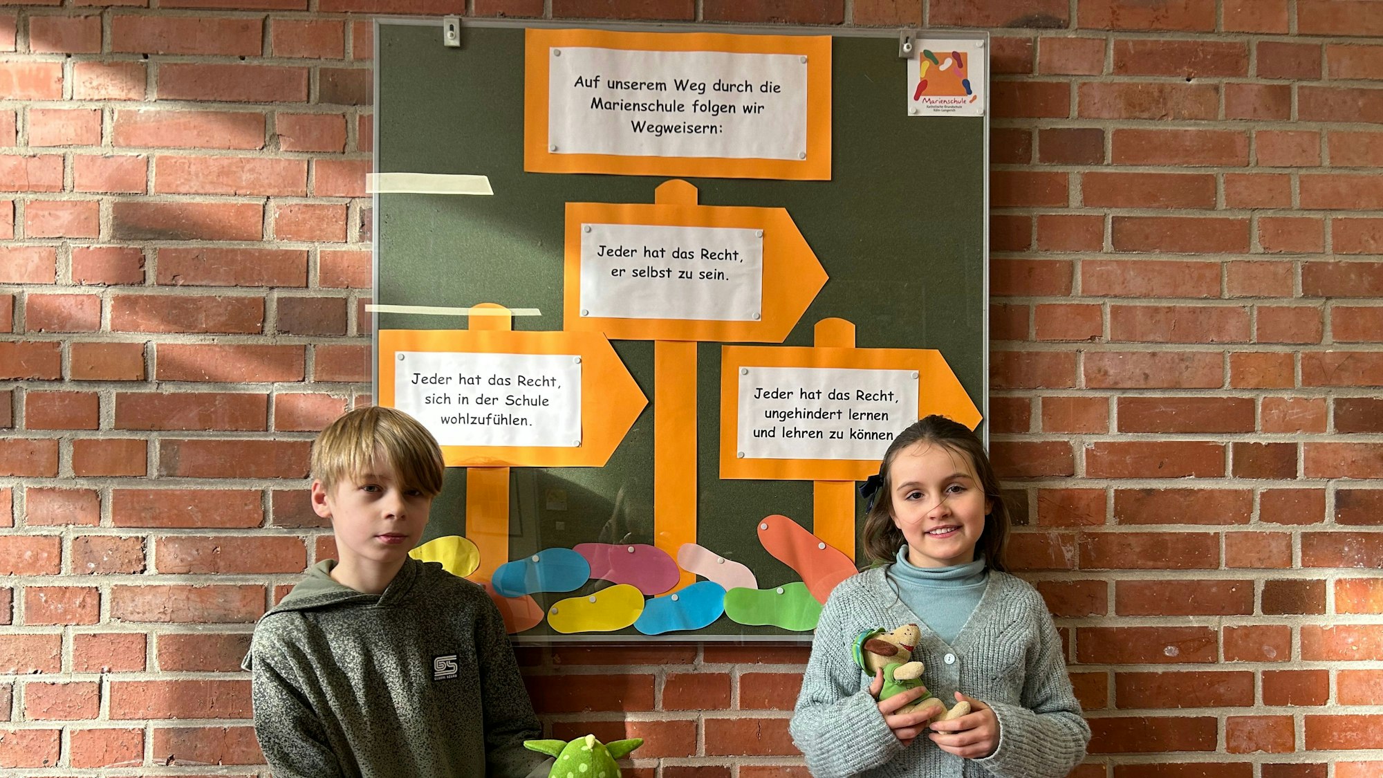 Die Schülersprecher Felix und Leonie (Name geändert) stehen vor einem Plakat über Kinderrechte in der Eingangshalle der Marienschule in Köln-Longerich.