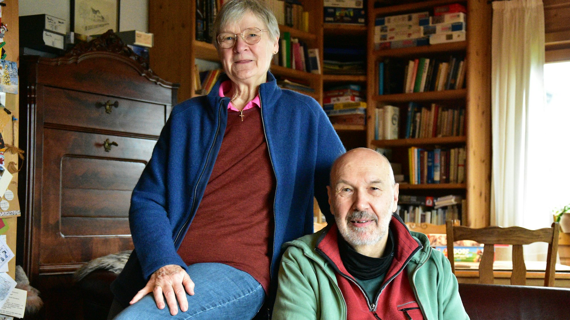 Ein Mann und eine Frau in einem Zimmer mit einem alten Schreibtisch und vielen Büchern. Sie sitzt auf der Lehne eines ledernen Sofas.