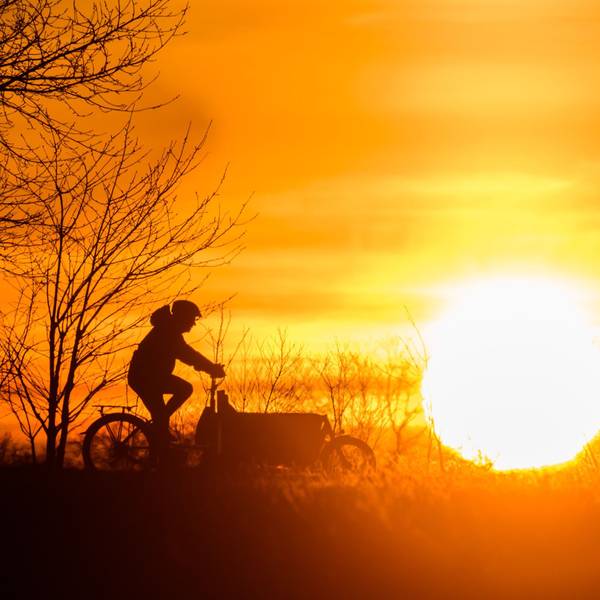 Ein Mann fährt bei Sonnenaufgang mit einem Lastenfahrrad über einen Feldweg in der Region Hannover.