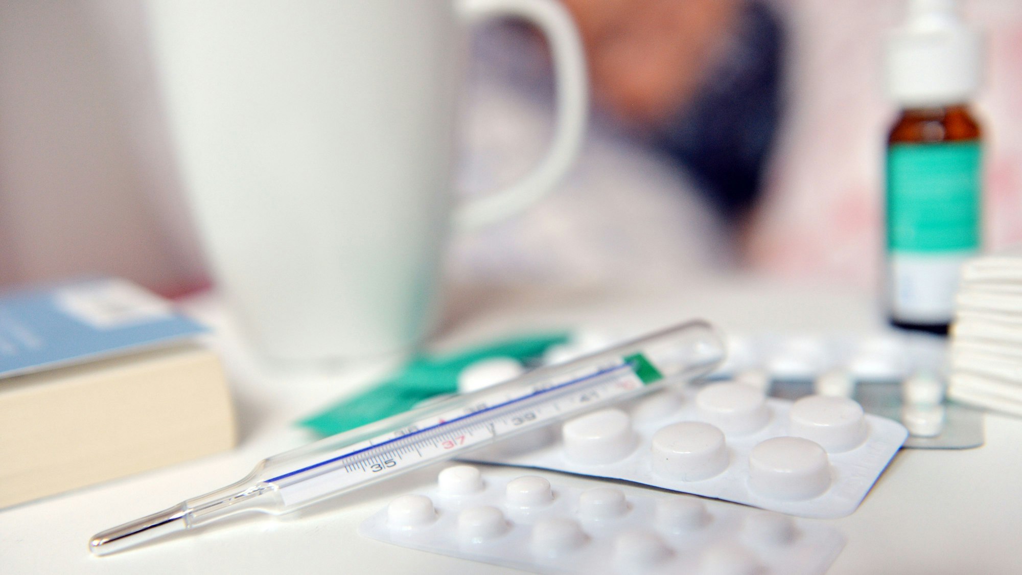 Medikamente und ein Fieberthermometer liegen auf einem Nachttisch.