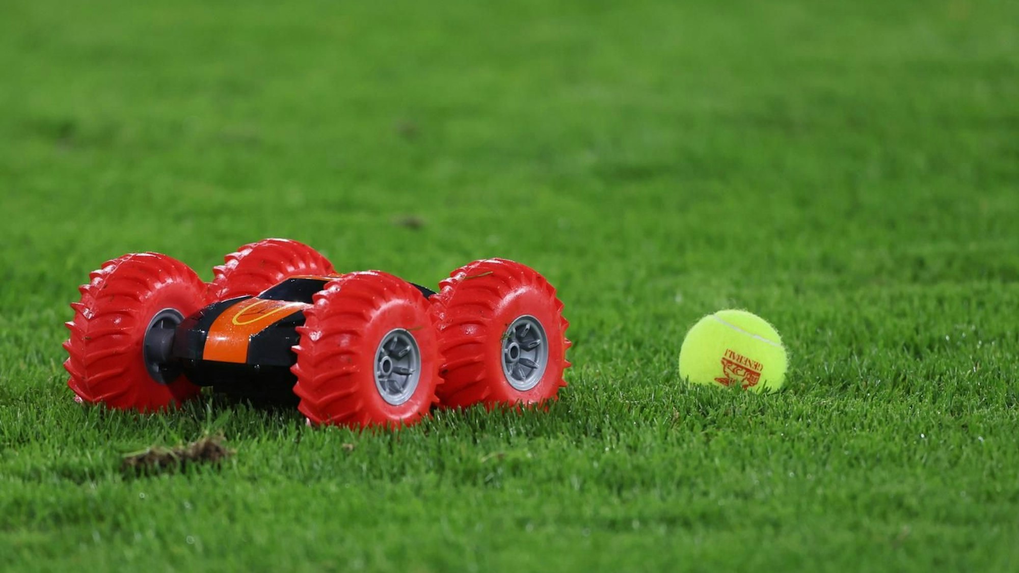 Ferngesteuertes Auto neben Tennisball auf dem Rasen