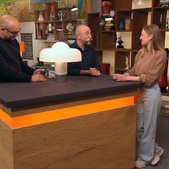 Experte Sven Deutschmanek (l.) nimmt bei „Bares für Rares“ die außergewöhnliche Lampe unter die Lupe. Horst Lichter (M.) staunte nicht schlecht über die Geschichte von Caroline Sauer (r.) aus Frechen.