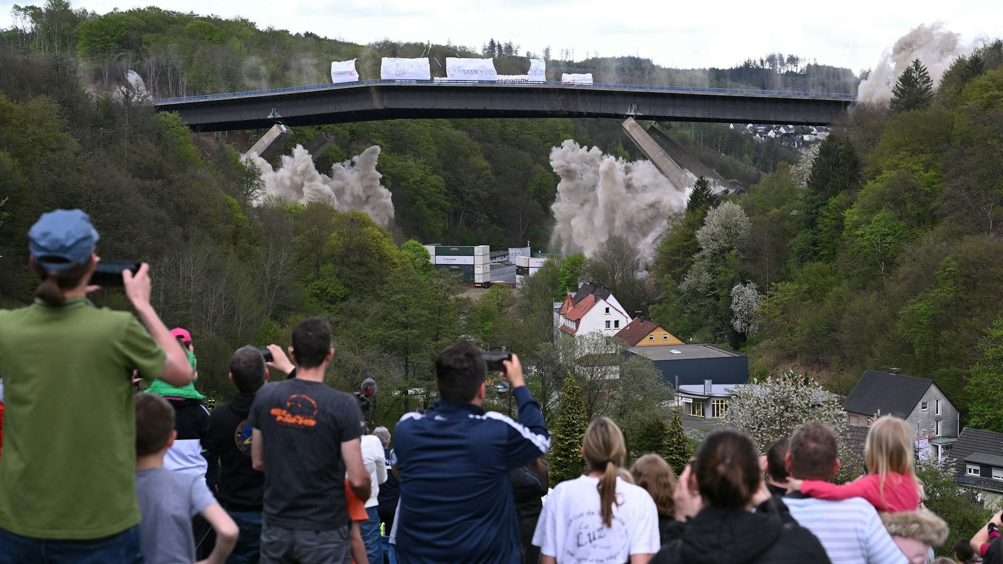 People take pictures of the Rahmede highway bridge during its blasting on May 7, 2023 on the A45 motorway, near Luedenscheid, western Germany.