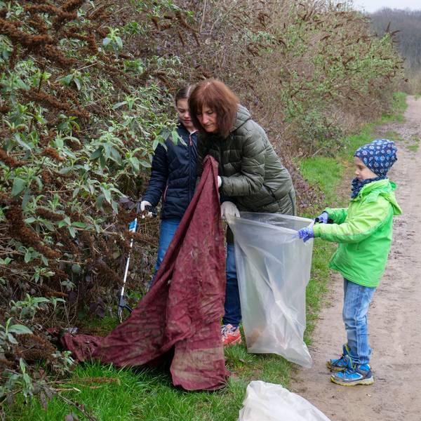 Auf dem Foto ist eine Frau mit zwei Kindern zu sehen, die Müll in einen Sack stopfen.
