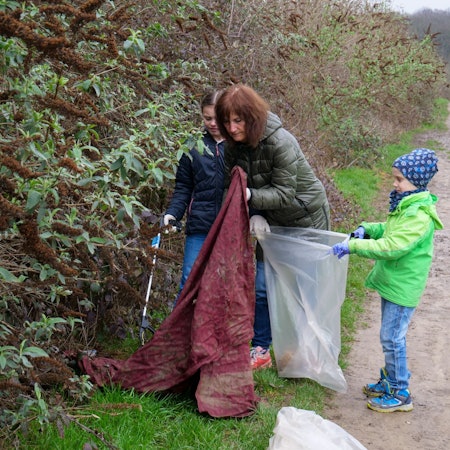 Auf dem Foto ist eine Frau mit zwei Kindern zu sehen, die Müll in einen Sack stopfen.