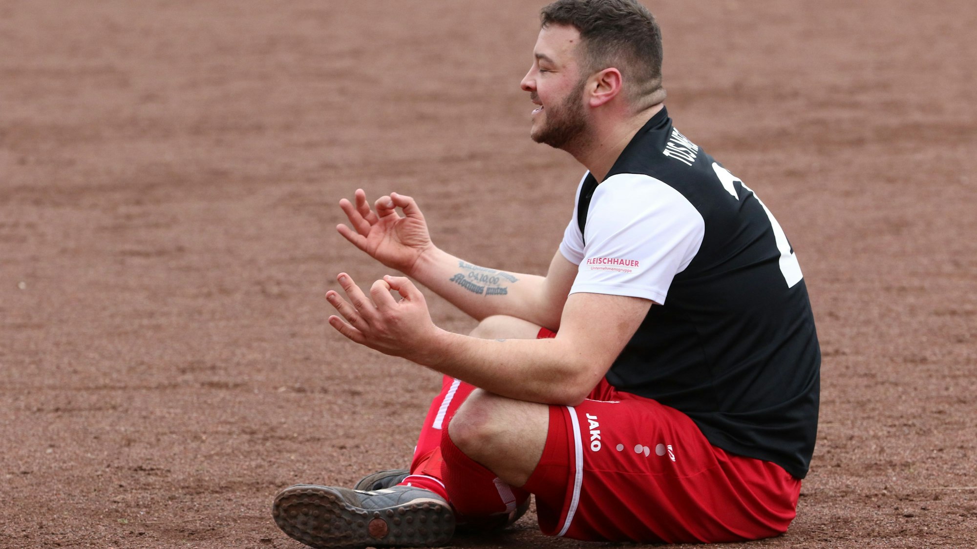 Oliver Zach sitzt wie einst Erling Haaland auf dem Boden und imitiert eine Meditation. Dabei grinst er über das ganze Gesicht.