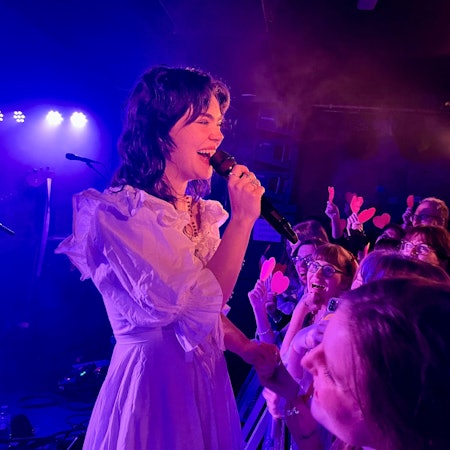 The Last Dinner Party am 17. Februar 2024 im Luxor, Sängerin Abigail Morris steht in einem weißen Kleid am Absperrgitter, Fans halten ihr rote Pappherzchen entgegen.