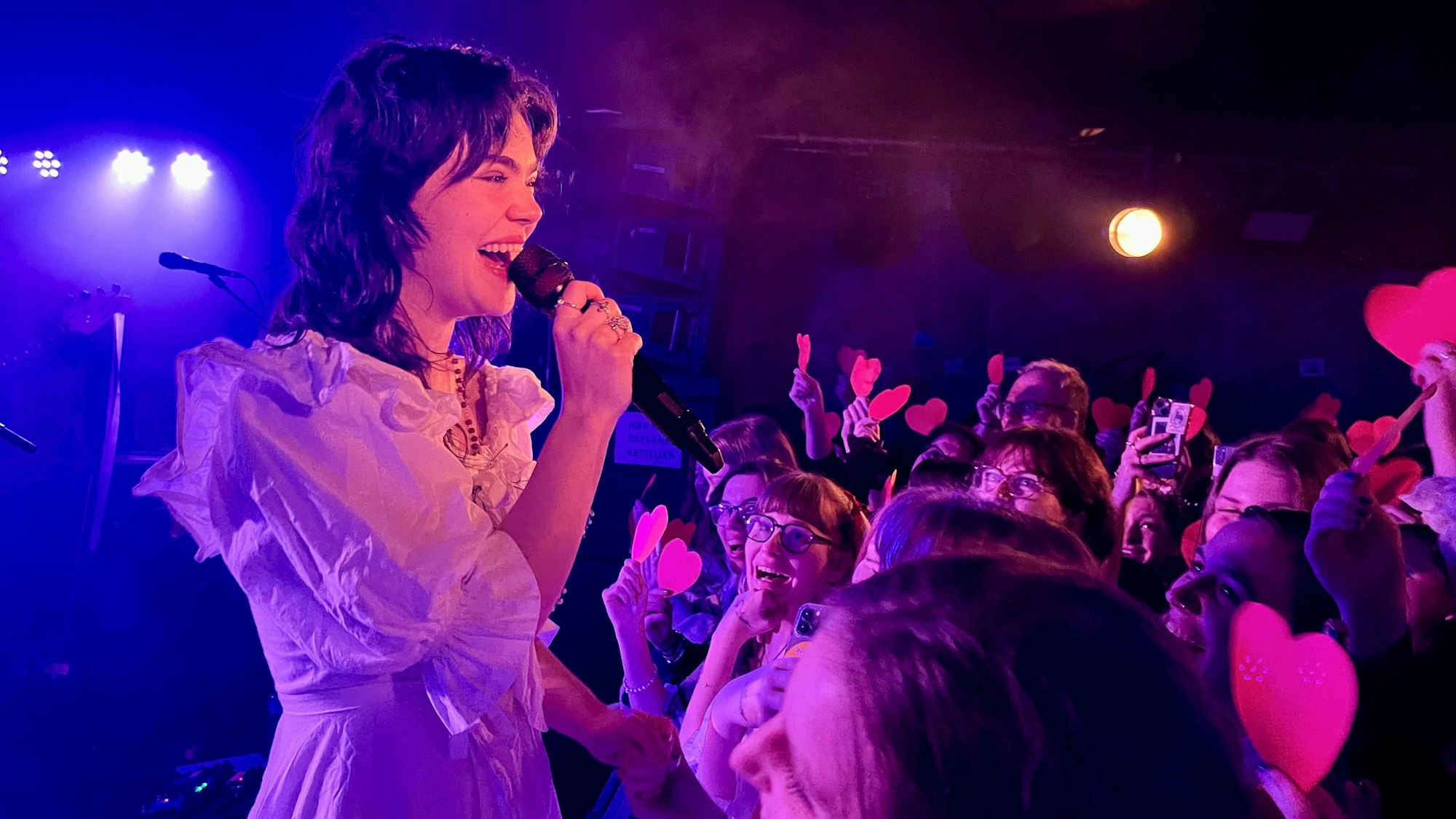 The Last Dinner Party am 17. Februar 2024 im Luxor, Sängerin Abigail Morris steht in einem weißen Kleid am Absperrgitter, Fans halten ihr rote Pappherzchen entgegen.