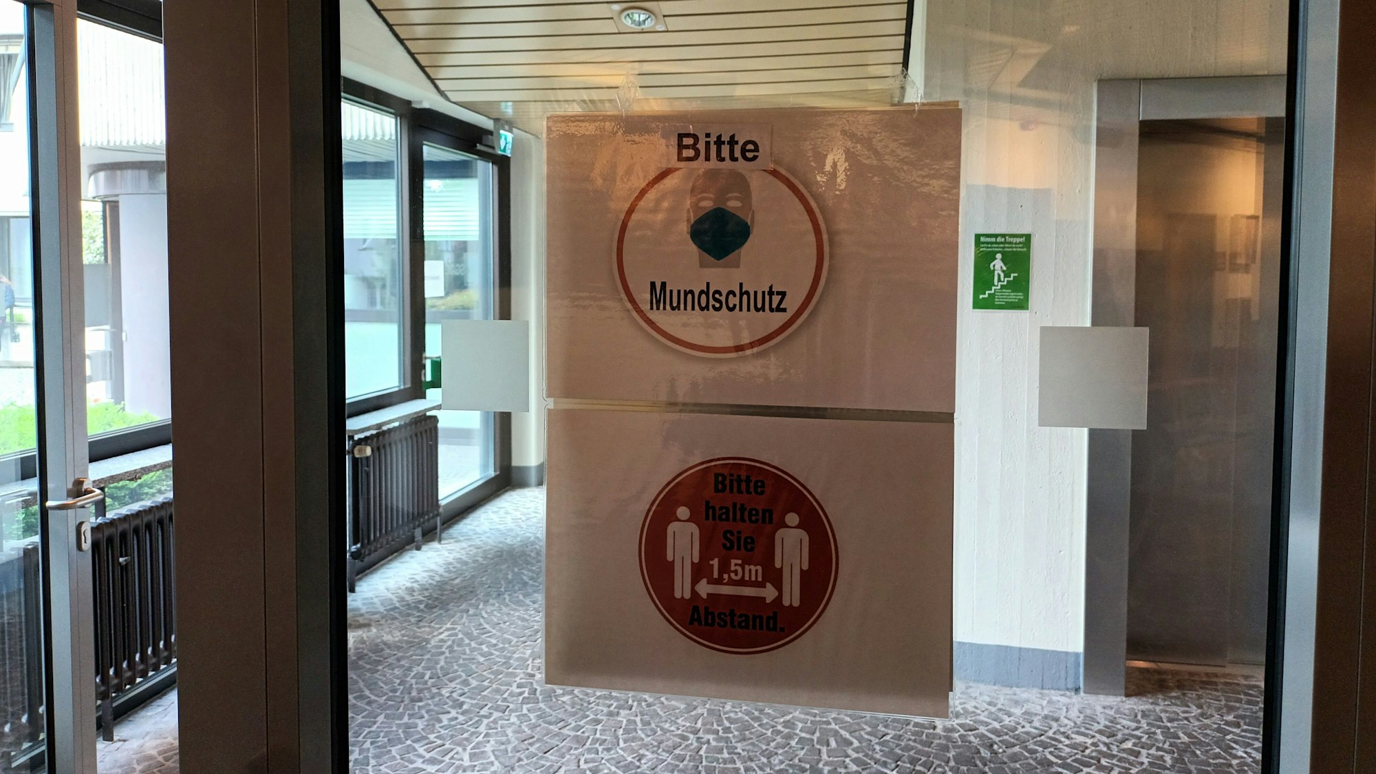 Schilder Bitte Mundschutz und Bitte Abstand halten hängen an einer Glastür