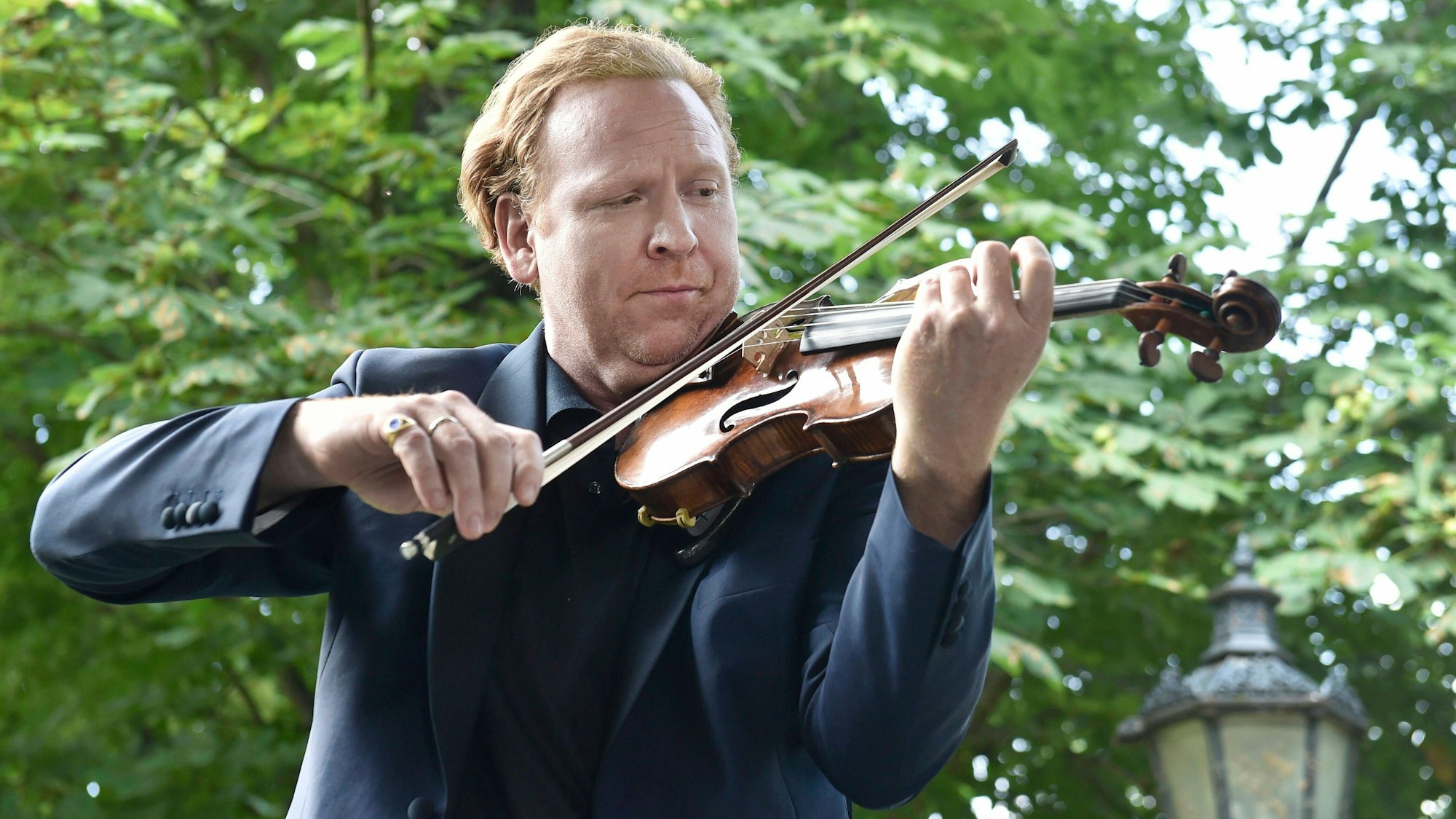 Daniel Hope steht in einem Garten und spielt Geige.