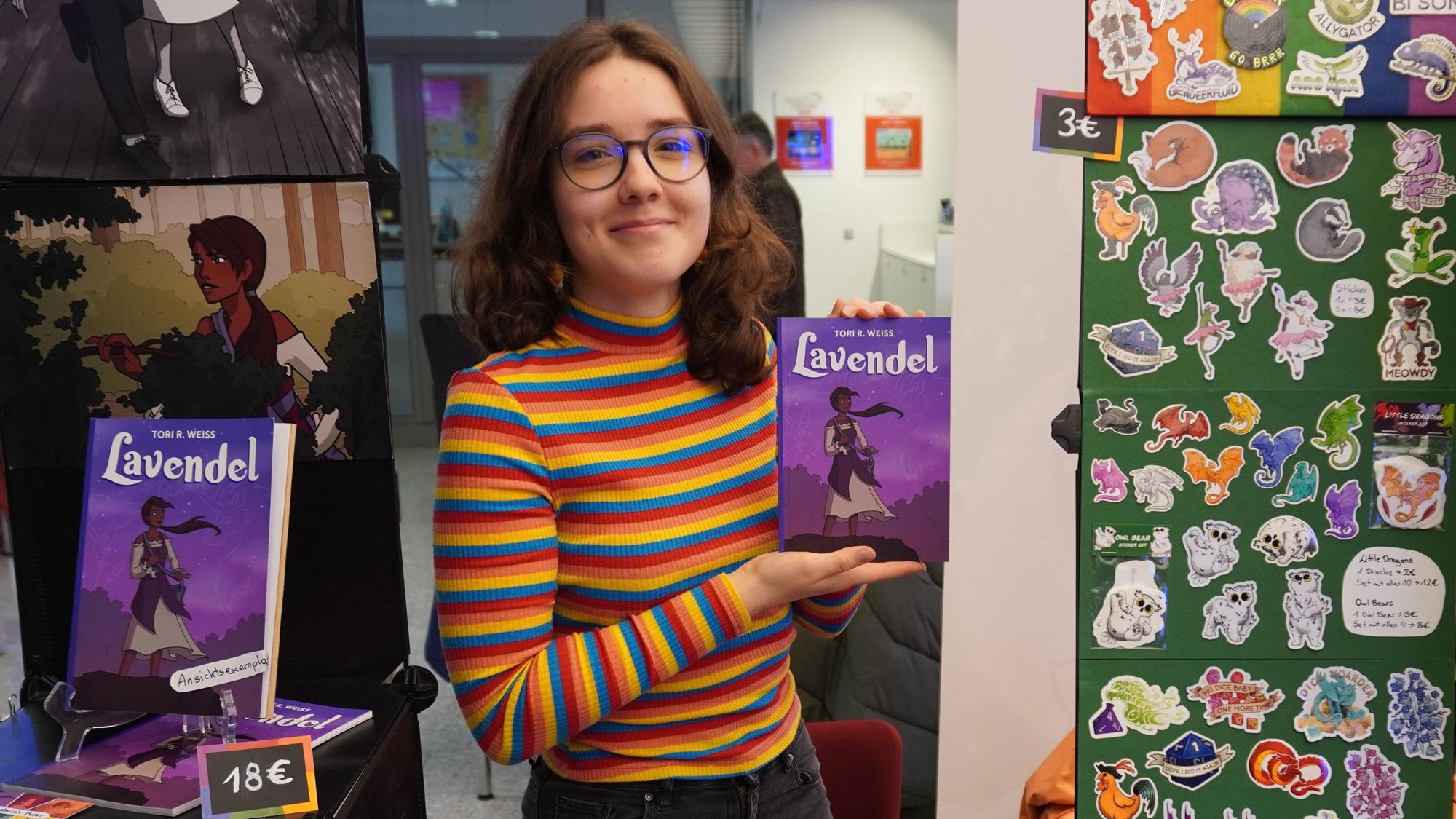 Auf dem Foto ist Tori Weiss zu sehen. Sie zeigt einen Comic, den sie im Selbstverlag herausgebracht hat.