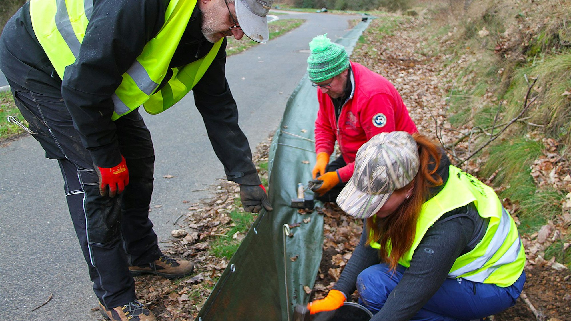 Drei Teilnehmer eines Nabu-Aktionstags bauen einen Schutzzaun für Amphibien auf. Zwei von ihnen tragen gelbe Warnwesten.